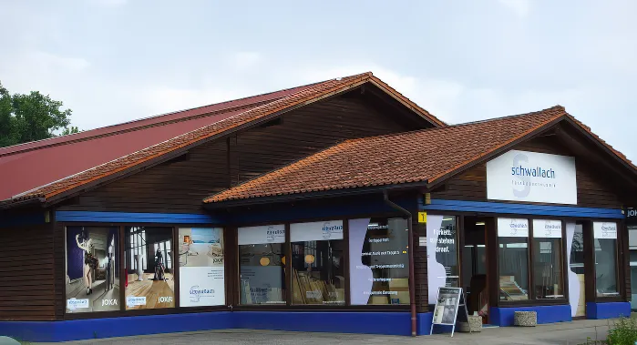 Firmengebäudegebäude - Fussbodentechnik Schwallach mit rotem Dach und blauen Zierleisten. In den Schaufenstern sind große Schilder und Anzeigen zu sehen. - Fussbodentechnik Schwallach -Bodenbeläge, Vinylbelag, Parkett - Neckaraue 7 - 71686 Remseck